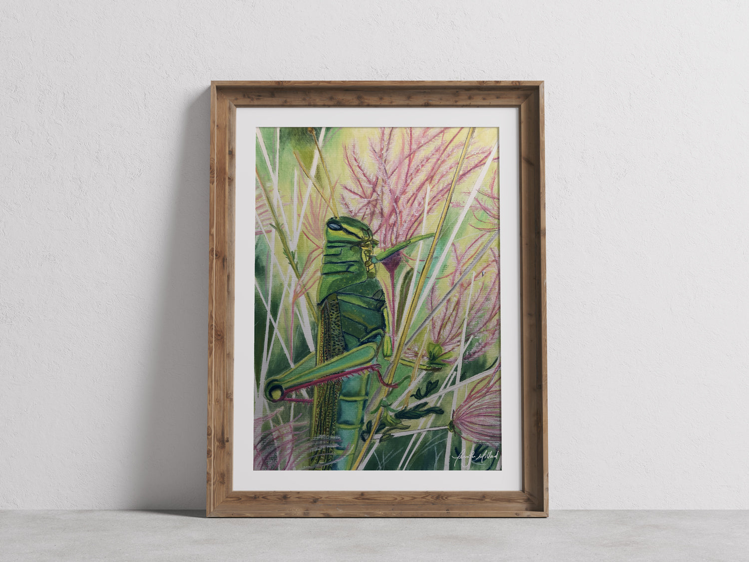 A giclee print of a bright green grasshopper in muhly pink grass in a wood frame with a white mat.