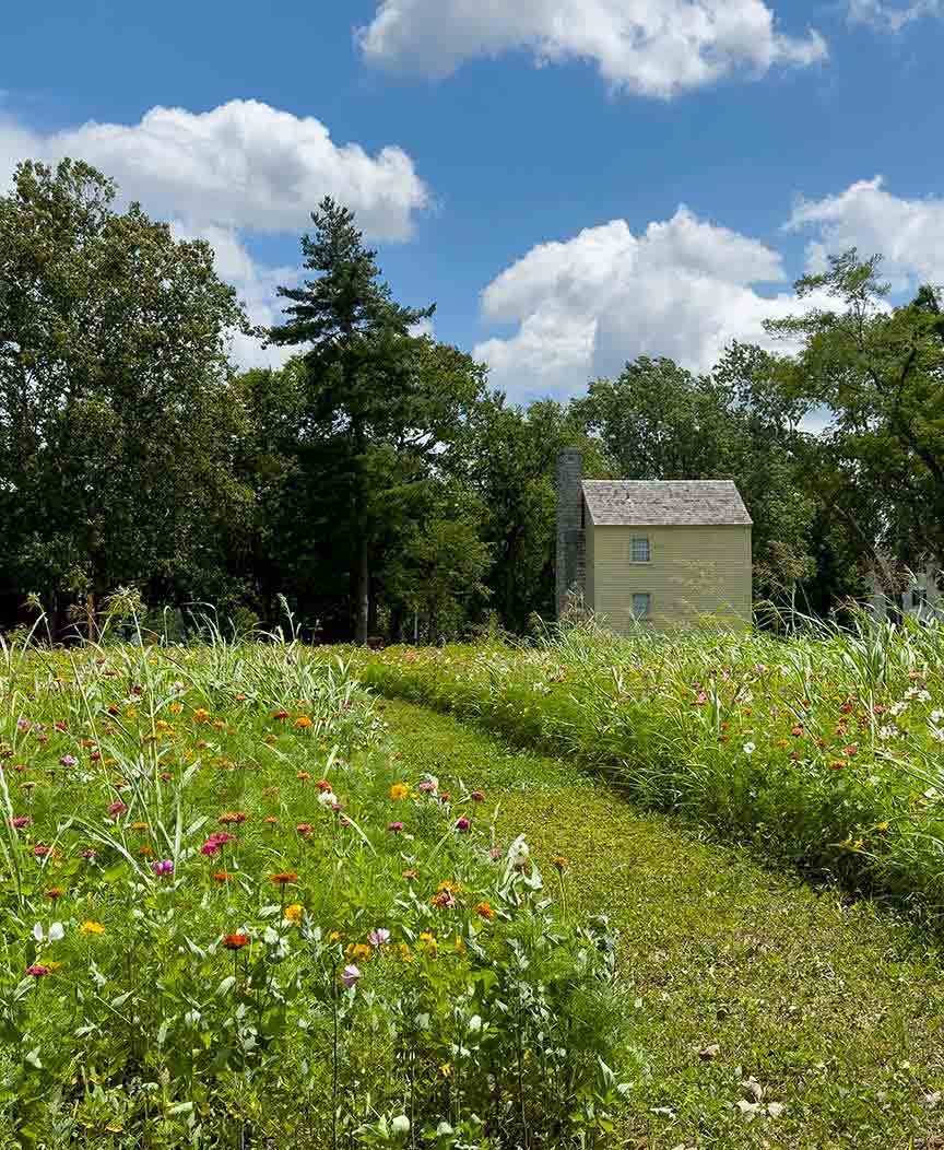 Photography of Shaker village's flower garden in the foreground and Shaker building in the background.