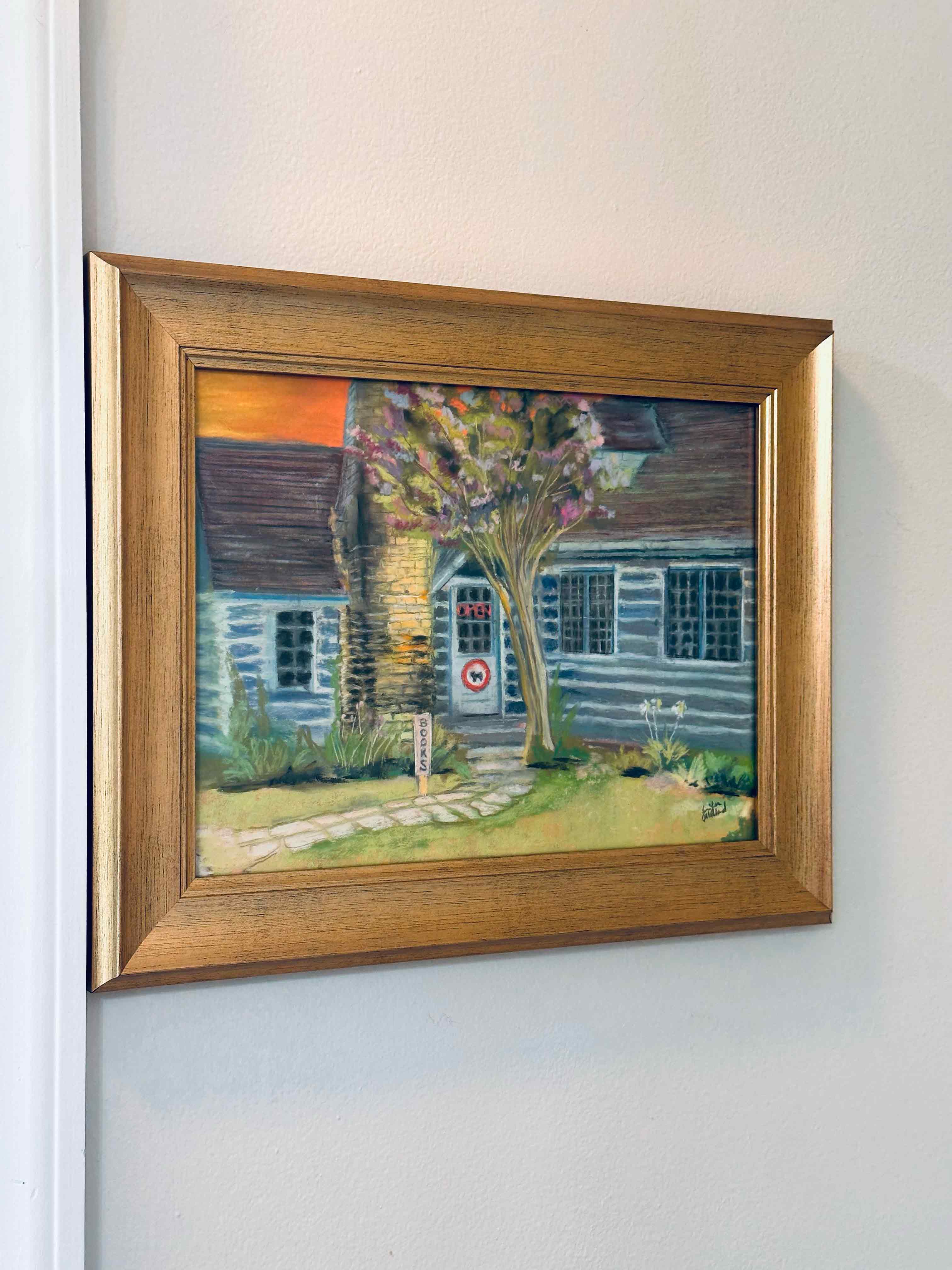 The soft pastel painting of the bookstore Taleless Dog in a gold frame.