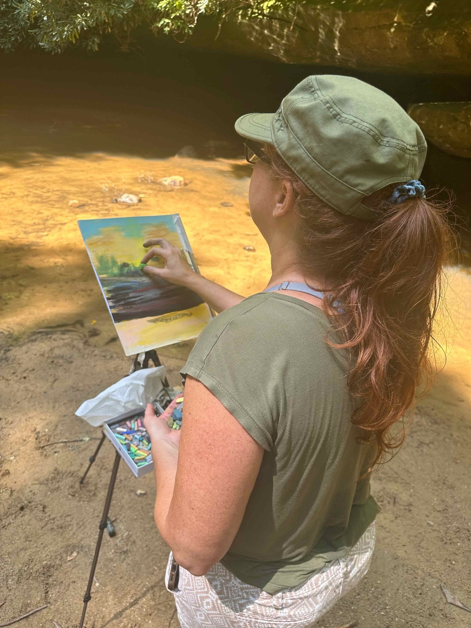A photo of the artist, Jennifer Millard, working outdoors at Creation Falls, painting the falls and pool of water below.