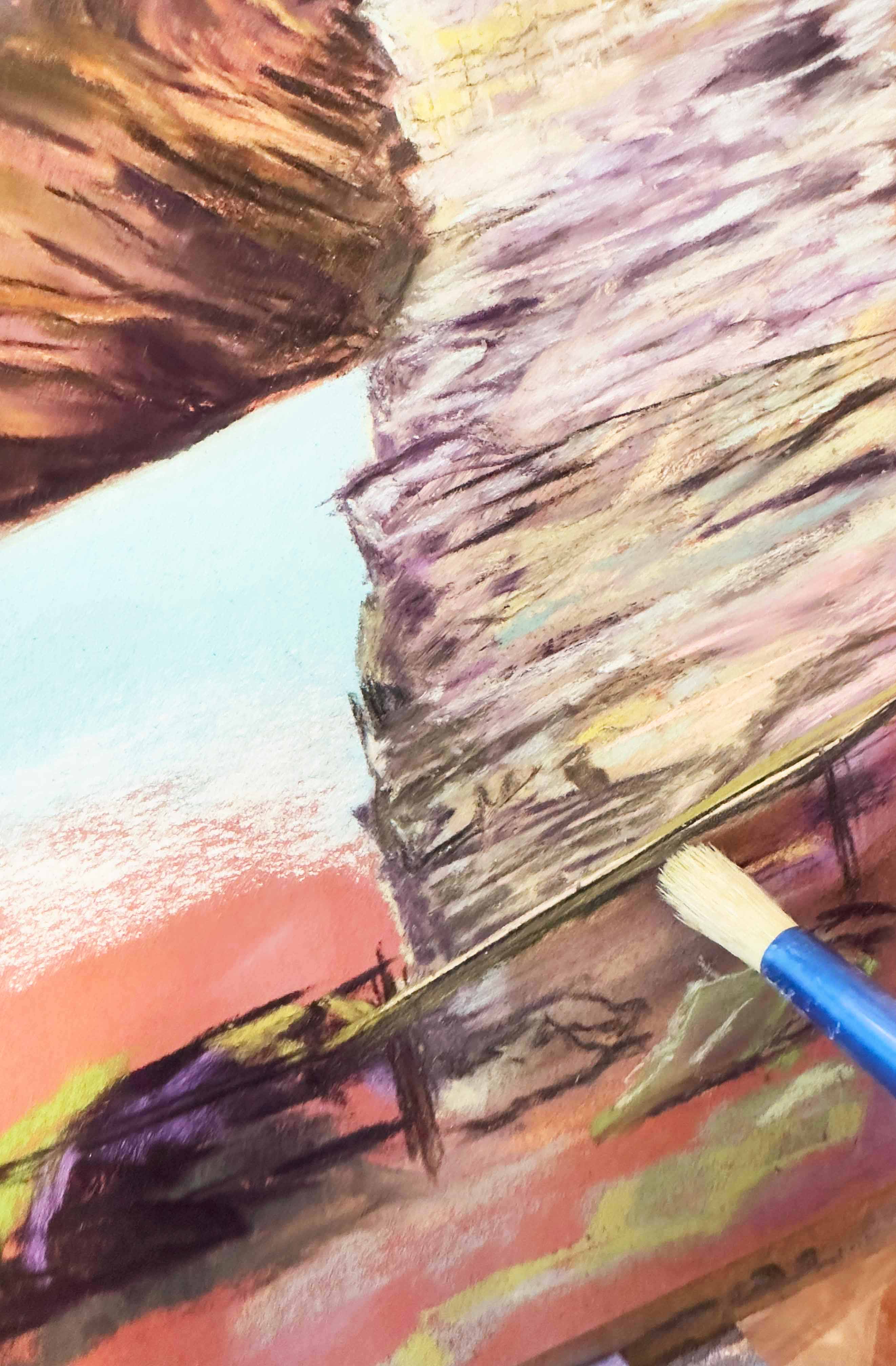 A photo of the artist using a stiff bristle brush to brush off some of the pastel color.