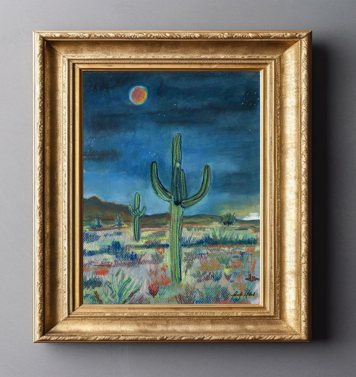 The desert at night in a giclee print of a soft pastel in an ornate gold frame. The colors are dark blues with highlights of orange reds.