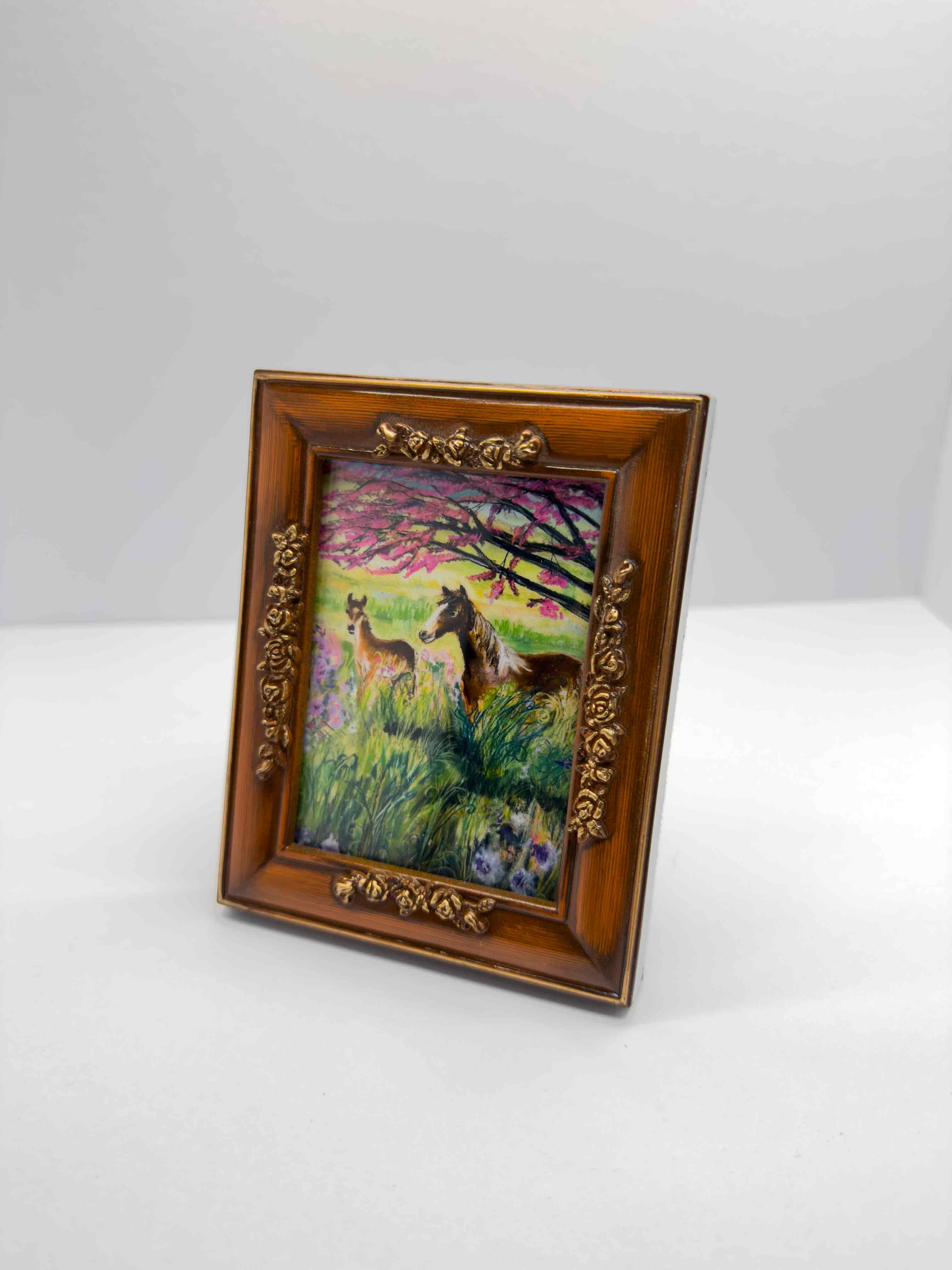 A Giclee print of a mama horse with her foal standing under a red bud tree in a vintage frame. 