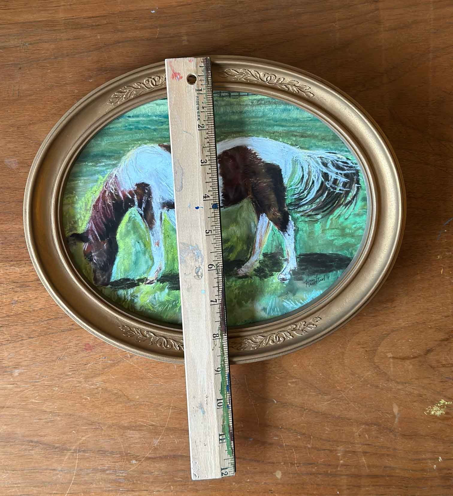A photo of a horse in a vintage gold oval frame is measured with a ruler to be almost 9" in height.